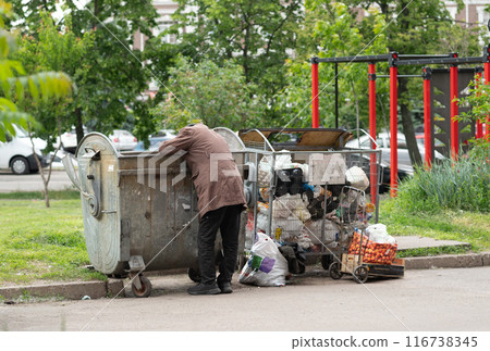 Hungry Man rummaging in trash container bin. Starving man looking for food in household rubbish Hungry Man rummaging in trash container bin. Starving man looking for food in household rubbish 116738345