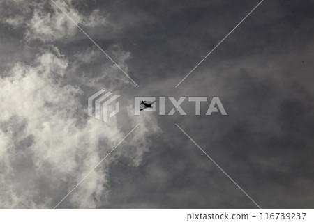 A small propeller plane flying high in the sky against a grey frowning sky and white smoke-like clouds. A gloomy picture. High quality photo 116739237