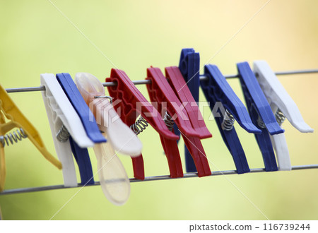 Multicoloured plastic clothes pegs hang from a clothes dryer on a green background. The metal fishing line is taut. Clothespin care. 116739244