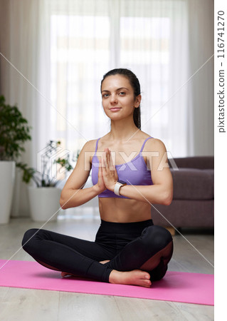 Caucasian woman practicing yoga and meditation sitting in lotus pose on pink yoga mat at home 116741270