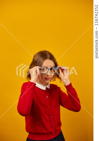 Teenage Girl in School Uniform Holding Glasses Against a Bright Yellow Background 116742352