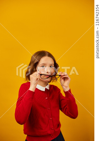 Teenage Girl in School Uniform Holding Glasses Against a Bright Yellow Background Teenage Girl in School Uniform Holding Glasses Against a Bright Yellow Background 116742354