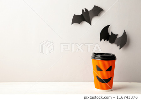 Paper cup with Halloween face in the grey background with halloween bats. 116743376