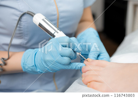 Podologist doing professional medical pedicure to young woman in the clinic. 116743803