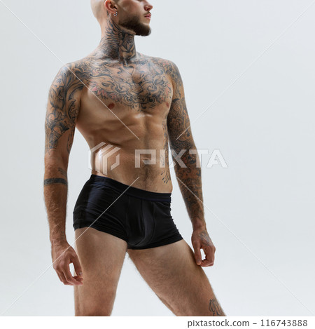 Cropped image of man with muscular, sportive body shape, tattooed, male model posing in black underwear isolated on white studio background Cropped image of man with muscular, sportive body shape, tattooed, male model posing in black underwear isolated on white studio background 116743888