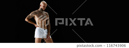 Handsome young bald man posing in white underwear, showing perfect muscular tattooed body against black studio background Handsome young bald man posing in white underwear, showing perfect muscular tattooed body against black studio background 116743906