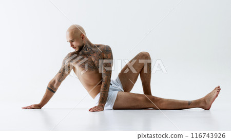 Handsome young bald guy with shirtless, tattooed muscular body posing in white underwear isolated on white studio background Handsome young bald guy with shirtless, tattooed muscular body posing in white underwear isolated on white studio background 116743926