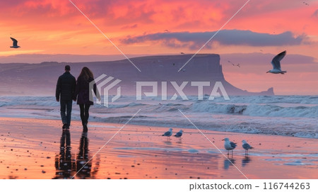 Romantic scene of a couple walking hand in hand along a serene beach at sunset, with soft waves lapping at their feet 116744263