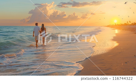 Romantic scene of a couple walking hand in hand along a serene beach at sunset, with soft waves lapping at their feet 116744322