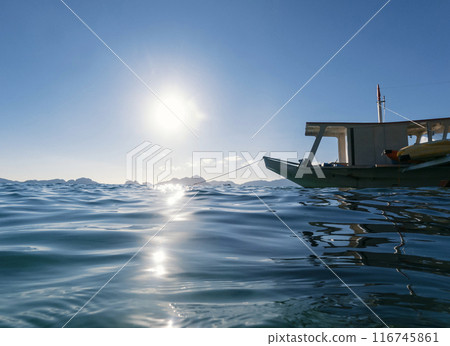 A small boat is moored in calm blue waters on a sunny day, with distant islands visible on the horizon. A small boat is moored in calm blue waters on a sunny day, with distant islands visible on the horizon. 116745861