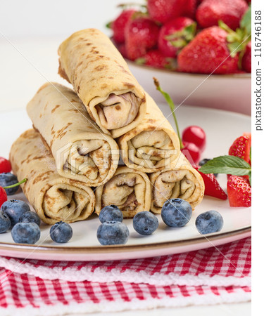 Stack of fried crepes with filling on a round plate, white table Stack of fried crepes with filling on a round plate, white table 116746188