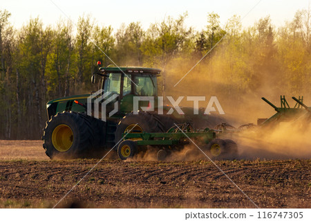 John Deere tractor and seeder working in the field in sunset. 116747305