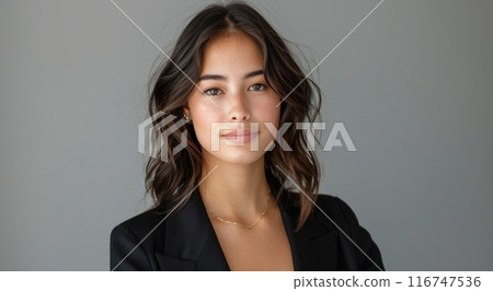 Young Woman Wearing Black Blazer and Necklace Against a Gray Wall 116747536