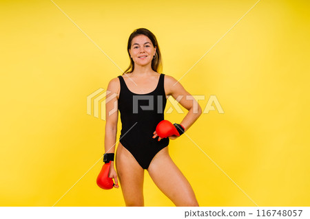 Strong sportswoman in boxing gloves prepared high kick. Isolated on white, red, yellow background 116748057