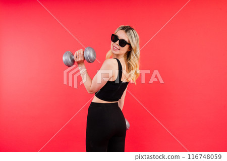 Young fitness trainer instructor wear black top hold dumbbells isolated on red background. Young fitness trainer instructor wear black top hold dumbbells isolated on red background. 116748059