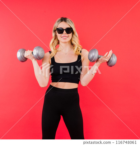 Young fitness trainer instructor wear black top hold dumbbells isolated on red background. 116748061