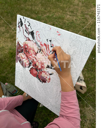 The woman writes a picture by numbers. Paints in numbered jars and a can of water. On open air. Close-up. 116748371