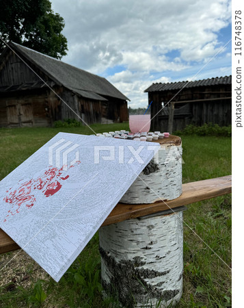 Rication for drawing by numbers on a stand. Paints in numbered jars and a can of water. Lying on a wooden bench. On open air. Rication for drawing by numbers on a stand. Paints in numbered jars and a can of water. Lying on a wooden bench. On open air. 116748378