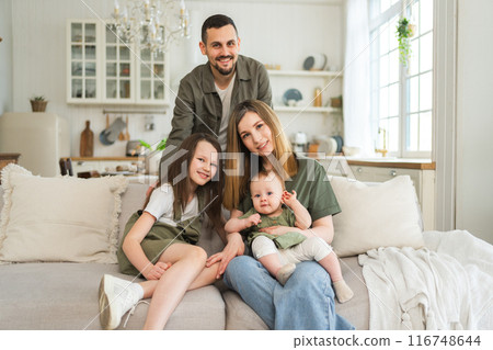 Happy family at home. Mother father two children daughters relaxing on sofa indoor. Mom dad parents baby girls kids relax playing having fun together. Family smiling laughing enjoying tender moment Happy family at home. Mother father two children daughters relaxing on sofa indoor. Mom dad parents baby girls kids relax playing having fun together. Family smiling laughing enjoying tender moment 116748644