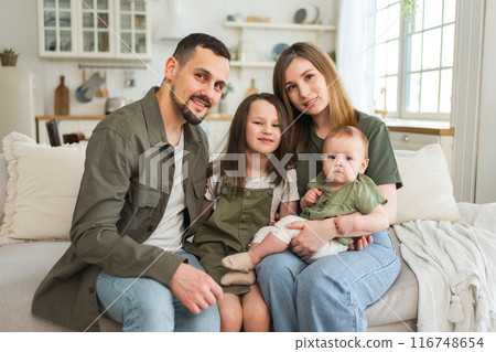 Happy family at home. Mother father two children daughters relaxing on sofa indoor. Mom dad parents baby girls kids relax playing having fun together. Family smiling laughing enjoying tender moment 116748654