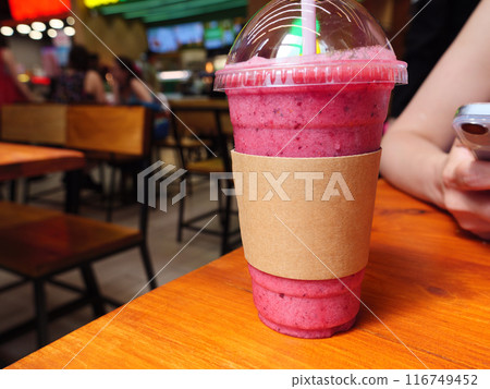 Pastic cup with a pink smoothie sits on a wooden table in the cafe Pastic cup with a pink smoothie sits on a wooden table in the cafe 116749452