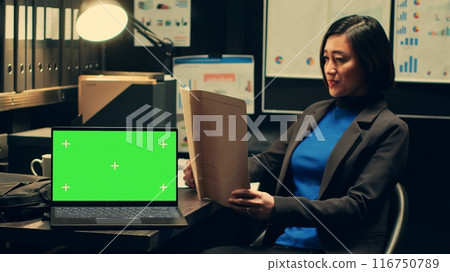 Private detective analyzing case files and uses greenscreen on pc, working on new investigation in archive room. Police officer reads archived folders, isolated chromakey template. Camera A. 116750789
