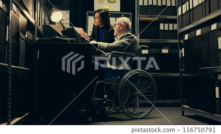 Inspector consulting with criminal expert on archived materials and autopsy records, examining folders and old cases to find connections. Private investigation in disability friendly space. Camera B. 116750791