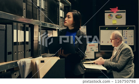 Detective evaluating old archived folders to organize all cases based on crimes, digitizes documents to preserve evidence on laptop. Private agent searching for forensics notes. Camera B. Detective evaluating old archived folders to organize all cases based on crimes, digitizes documents to preserve evidence on laptop. Private agent searching for forensics notes. Camera B. 116750798