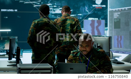 In a high tech military office, soldiers team analyze real time data collected by surveillance system. Staff interpret intelligence and coordinate operations to ensure national defense. Camera A. 116750840