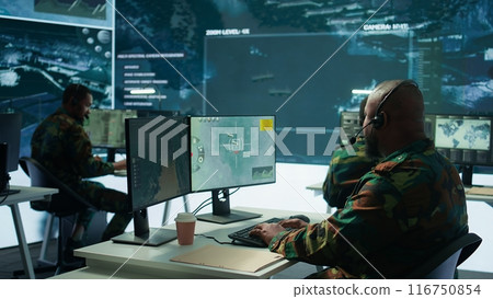 Military personnel in a base of operations using advanced computers and big screen, monitoring satellite systems to enhance security measures and process data. High tech army gear. Camera B. Military personnel in a base of operations using advanced computers and big screen, monitoring satellite systems to enhance security measures and process data. High tech army gear. Camera B. 116750854