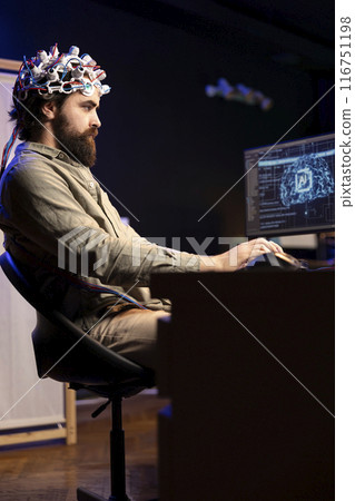 Programmer using EEG headset translating thoughts into PC commands using brainwave signals. Man controlling computer functions using his mind, helped by biosensor technology research Programmer using EEG headset translating thoughts into PC commands using brainwave signals. Man controlling computer functions using his mind, helped by biosensor technology research 116751198