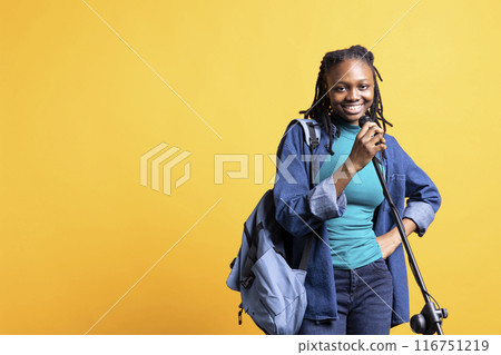 Radiant teenager holding microphone, performing songs in concert, isolated over studio background. Upbeat talented vocalist singing to spectators using mic, doing karaoke, having fun 116751219