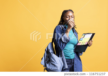 African american teenager enjoying coffee while examining clipboard with colorful sticky notes. BIPOC young person doing productivity tasks, drinking caffeinated beverage, studio background African american teenager enjoying coffee while examining clipboard with colorful sticky notes. BIPOC young person doing productivity tasks, drinking caffeinated beverage, studio background 116751237