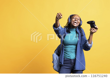 Euphoric african american teenager playing intense gaming console game, celebrating win, studio background. Ecstatic BIPOC young girl using controller, excited after being victorious in videogame Euphoric african american teenager playing intense gaming console game, celebrating win, studio background. Ecstatic BIPOC young girl using controller, excited after being victorious in videogame 116751240