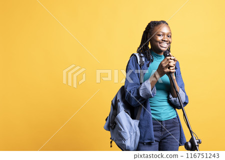 Portrait of smiling young presenter with backpack talking in microphone, addressing audience, studio background. Jolly school council president using mic, doing speech for students Portrait of smiling young presenter with backpack talking in microphone, addressing audience, studio background. Jolly school council president using mic, doing speech for students 116751243