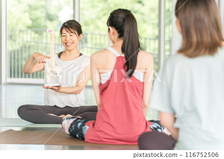 A female yoga instructor gives guidance on improving posture using a pelvis, tailbone, and skeletal model 116752506