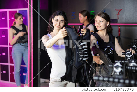 Girls try on a matching vest for playing laser tag in dark room Girls try on a matching vest for playing laser tag in dark room 116753376