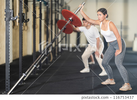 Athletic young woman pumping up her arm biceps using one side of barbell Athletic young woman pumping up her arm biceps using one side of barbell 116753437