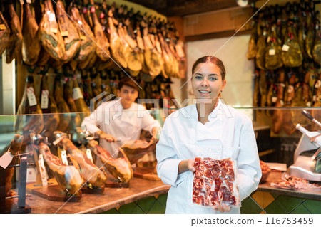Young salesgirl of butcher shop offering package of sliced Iberian jamon 116753459