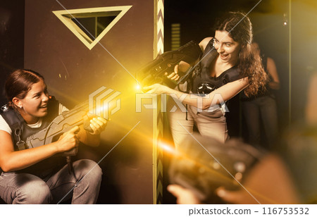 Portrait of excited girlfriends playing enthusiastically laser tag game two teams opposite each other in room Portrait of excited girlfriends playing enthusiastically laser tag game two teams opposite each other in room 116753532