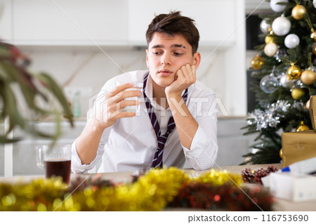 Young lonely man drinking alcohol at christmas table at home 116753690