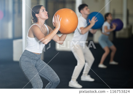 Crossfit in the gym - young people throwing a ball into hoop Crossfit in the gym - young people throwing a ball into hoop 116753824