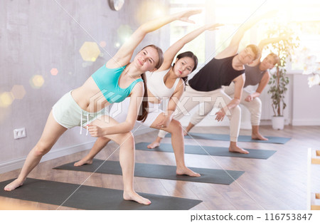 Slim young girl practicing extended side angle pose of yoga on black mat 116753847