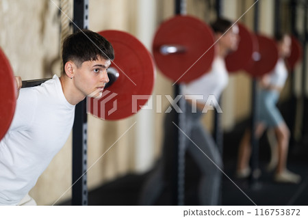 Young guy doing exercises with a barbell in gym Young guy doing exercises with a barbell in gym 116753872