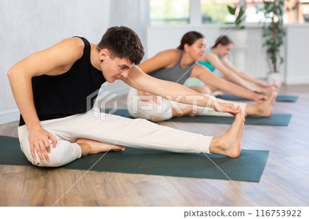 Yoga class of sports women and man performing Head to Knee Forward Bend Pose, or Janu Sirsasana after practicing together 116753922