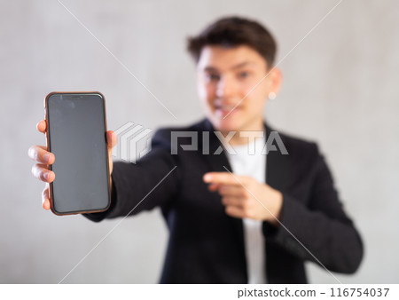 Unfocused agent in suit jacket shows dark empty mobile phone screen and points at device with hand 116754037