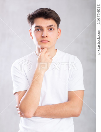 Thoughtful young man standing against background of grey unicolored wall 116754058