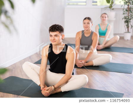 Young man practicing butterfly pose of yoga in light fitness room 116754093