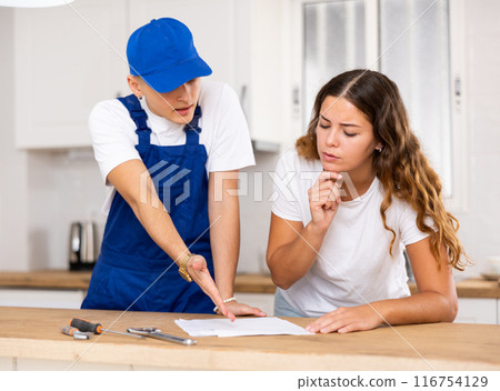 Positive plumber tells an young housewife where to sign an invoice for work performed. 116754129