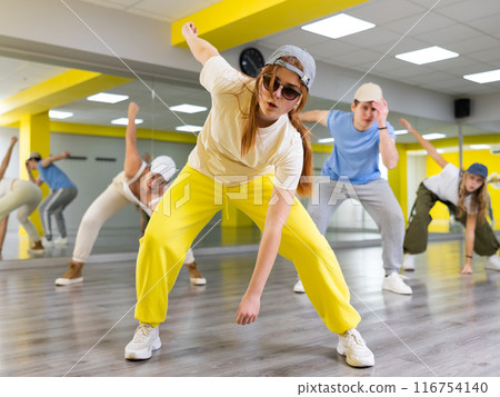 Excited positive teenage dancers having fun and learning modern dance during class in modern hall 116754140